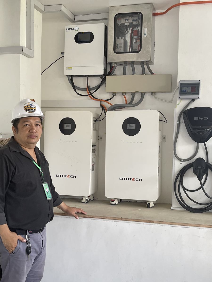 SolarWave technician beside a wall-mounted hybrid inverter and two lithium battery units