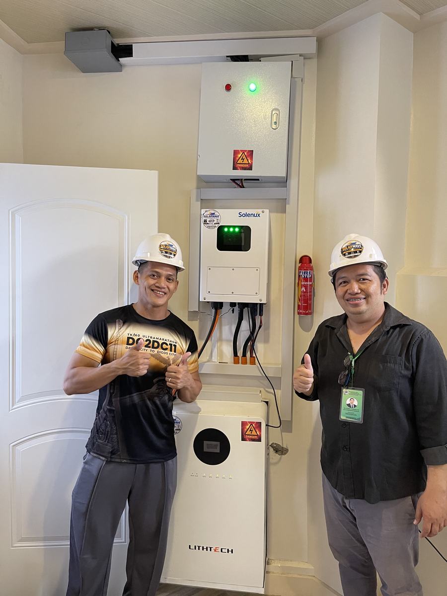 Two SolarWave crew members giving a thumbs up beside a completed inverter and battery install